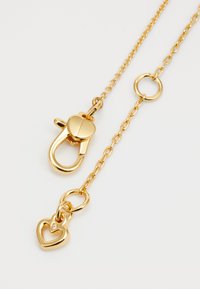 Zlato obarvana veriga z mehanizmom za zapiranje v obliki zavrtnja in obeskom v obliki srca, ki vsebuje majhen dragulj. Ima teksturirane povezave in okroglo obrobo.
