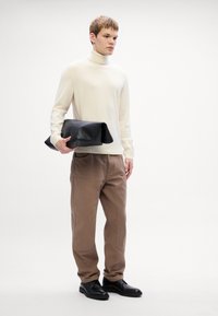 Pulover bej deschis cu guler înalt, pantaloni bordeaux cu croială lejeră, poșetă din piele neagră pliată și pantofi negri pe un fundal simplu.