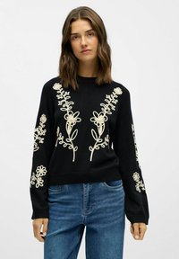 Pull noir en tissu doux, orné d'une broderie florale crème complexe sur le devant et les manches. Encolure ras du cou et coupe décontractée.