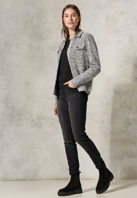 Grau gestreifte Jacke im Fischgrätenmuster mit einem Kragen, kombiniert mit einem schwarzen Oberteil, schwarzen Skinny-Jeans und schwarzen Stiefeletten.