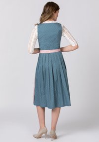Dirndl dress in teal with white polka dots, features a pink waistband and pleated skirt. Back view shows a fitted bodice and lace-sleeved blouse.