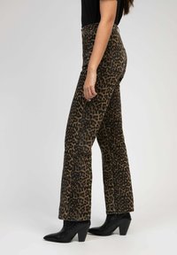 Pantalons taille haute à imprimé léopard en tissu texturé, présentant une coupe évasée et des poches cousues, associés à des bottes à talons noires.