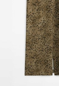 Tissu brun avec un motif de points noirs éclaboussés. Texture lisse avec une coupe droite, comportant une fente sur un côté.
