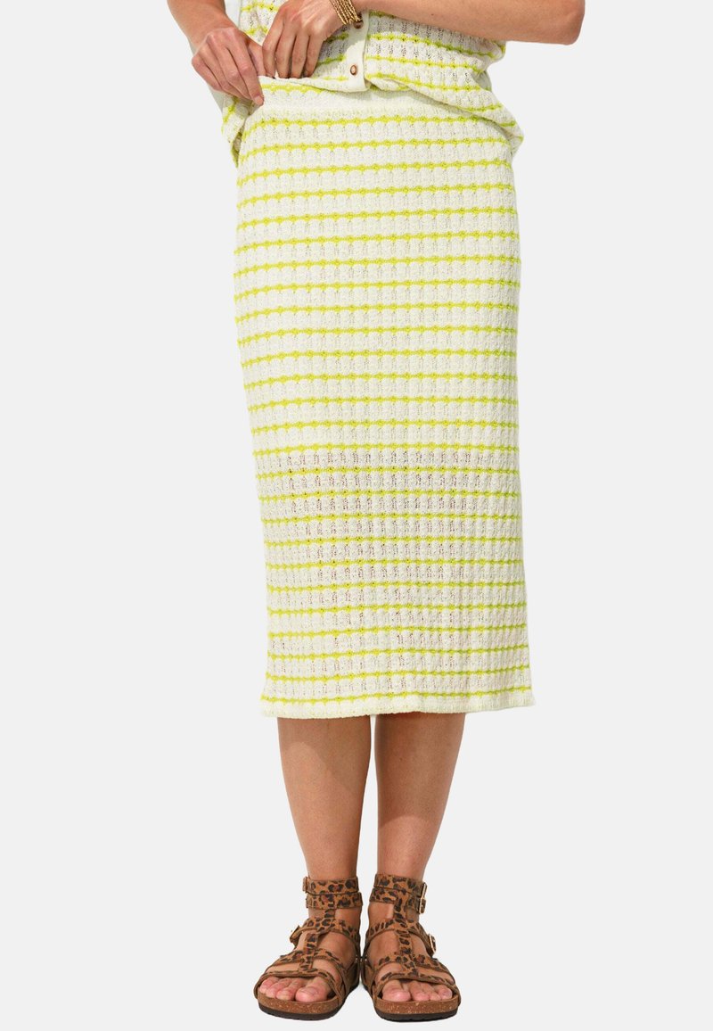 Jupe crayon en tricot avec des rayures blanches et jaunes fluo alternées, tissu texturé, et longueur mi-mollet. Assortie avec des sandales brunes à lanières.