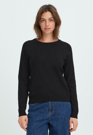 Svart strikkegenser med lange ermer, rund hals og ribbestrikket kant i avslappet passform. Kombinert med denimjeans, mot en lys bakgrunn.