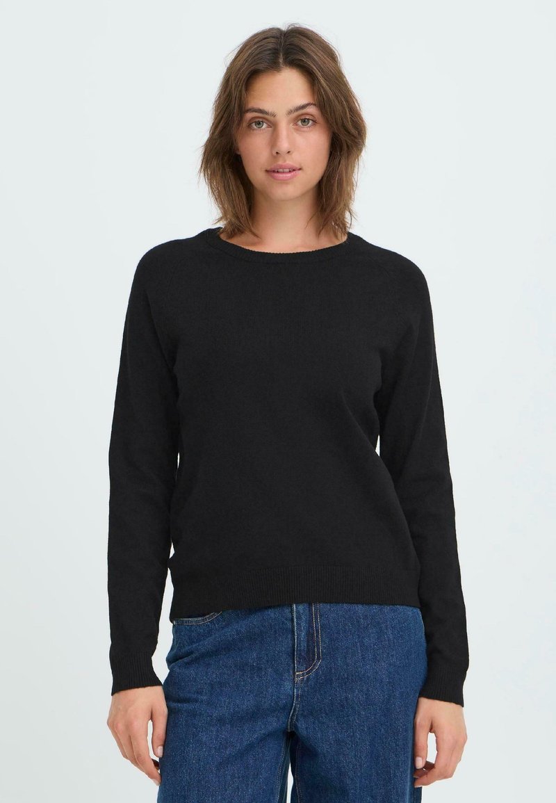 Zwarte gebreide trui met lange mouwen, ronde hals en geribde zoom in een relaxte pasvorm. Gecombineerd met denim jeans, tegen een lichte achtergrond.