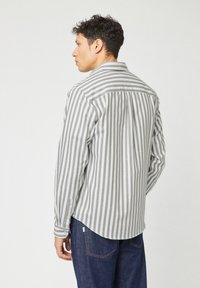 Camicia a maniche lunghe grigio e bianca a righe con orlo curvo, polsini con bottoni e una singola cucitura sulla parte posteriore, realizzata in tessuto leggero.