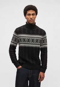 Čierny pletený rolákový sveter s vrkočovým vzorom a bielym geometrickým motívom na hrudi. Pritiahnuté manžety a pás.