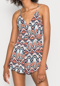 Rompers sans manches au motif multicolore vif avec un décolleté en V profond et une taille élastique. Le tissu est lisse avec une coupe fluide.