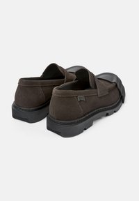Mocasines de ante marrón oscuro con suela de goma negra. Presentan detalles cosidos y un diseño superior suave, adecuados para un uso casual.