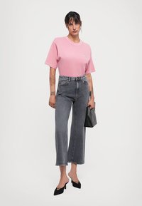 Pink short-sleeve t-shirt, high-waisted dark gray straight-leg jeans, black stiletto heels, and a black handbag. Plain background.