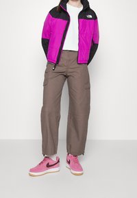 Fialová a černá péřová bunda, béžové cargo kalhoty a růžové tenisky Nike Air Force 1. Oblečení má ležérní design s výraznými barevnými bloky.