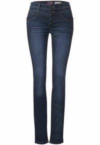 Tummansinisten farkkujen ohuempi malli, jossa on kaksi etutaskua ja nappisuljenta erottuvilla ompeluyksityiskohdilla.