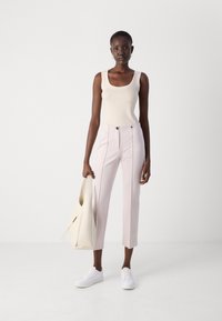 Beige tanktop, lichtroze op maat gemaakte broek met zijpijpen en twee voorknopen, gecombineerd met witte sneakers en een crèmekleurige handtas.