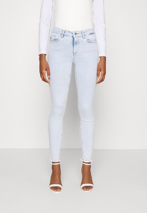 Jeans skinny bleu clair avec une finition délavée, cinq poches et un ourlet effiloché. Associés à des sandales blanches à lanières. Texture en denim lisse.