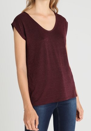 Vrouw draagt een donkerbordeauxroze gebreide top met korte mouwen en een V-hals met een subtiele glans, gecombineerd met donkerblauwe nauwsluitende jeans.