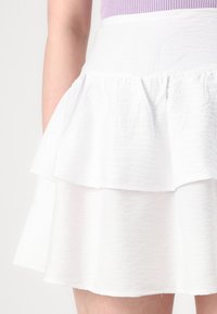 Hvit lagdelt skjørt laget av teksturert stoff, med en flagrende design og to volanglag, samt elastisk midjebånd.