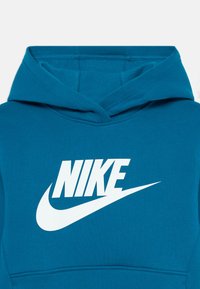 Tīra zaļā kapuce ar baltu Nike logo. Ar lielu kabatu un savelkamu kapuci. Gluda struktūra ar izšūtām detaļām.