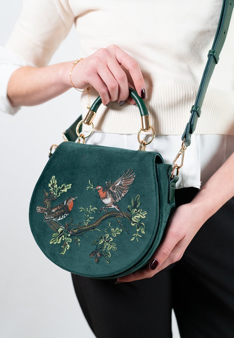 Grön mockaväska med cirkulär form, prydd med broderade fåglar och blad. Guldiga detaljer och en avtagbar rem.
