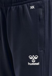 Marineblaue Jogginghose mit elastischem Bund, seitlichen Taschen und weißem "hummel"-Logo mit dekorativem Emblem in der Hüfthöhe. Weiche Stofftextur.