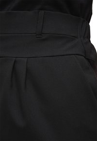 Pantalons noirs ajustés avec une texture lisse, présentant une large taille, des plis et des détails de coutures subtils.