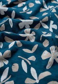 Modra tkanina z bežnimi abstraktnimi cvetličnimi in listnatimi vzorci, ki prikazuje mehke gube in teksturo.