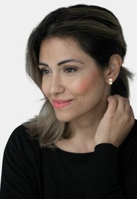 Orecchini a bottone dorati con un design rettangolare e dettagli sottili. Indossati da una donna con capelli scuri di lunghezza media.