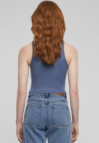 Skrajšan modri top s ozkimi naramnicami, ki ima rebrasto teksturo. V kombinaciji z visokim pasom, svetlim modrim džinsom z dvema žepoma na hrbtni strani.
