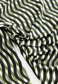 Tessuto con motivo verde e nero caratterizzato da linee ondulate, con una texture liscia e una leggera lucentezza, piegato per una presentazione dinamica.