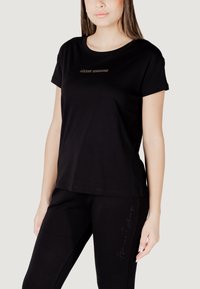 T-shirt nera in cotone con maniche corte e scollo tondo, dotata di un logo dorato stampato al centro. Abbinato a pantaloni neri con dettagli laterali.