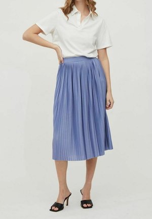 Kvinde iført en hvid kortærmet polo-shirt, en højtaljet blå midi plisseret nederdel og sorte åbne hælede sandaler.