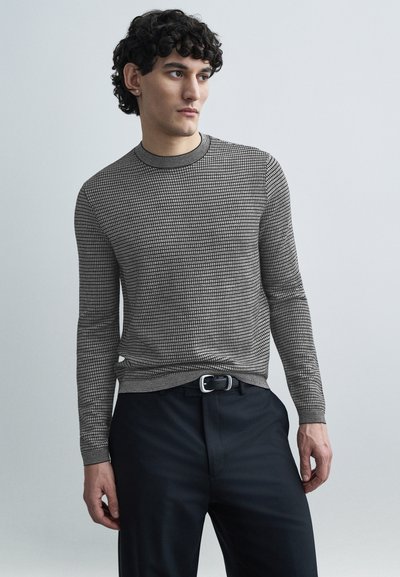 Pull en maille à manches longues noir et blanc avec un motif géométrique, col rond et poignets côtelés, associé à un pantalon sombre ajusté.
