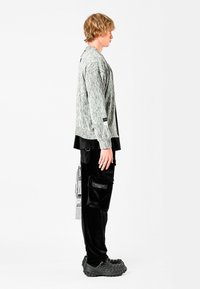 Suéter gris texturizado con acentos negros, combinado con pantalones cargo de pana negros con bolsillos. Calzado negro completa el aspecto.