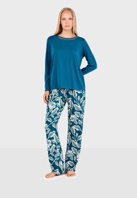Chemise à manches longues de couleur teal avec un col arrondi, associée à un pantalon bleu à jambe large orné d'un motif floral blanc. Tissu doux, coupe décontractée.