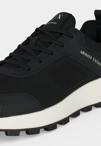 Κοντινό ενός μαύρου sneaker Armani Exchange με μαύρα κορδόνια, υφή στα πλαϊνά και λευκή σόλα με τραχιά υφή.