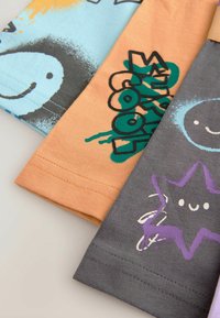 Trzy złożone T-shirty: jasnoniebieski z uśmiechem, pomarańczowy z napisem "cool" oraz szary z fioletową gwiazdą, wszystkie wykonane z bawełny z graficznymi nadrukami.