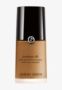 Giorgio Armani Luminous Silk -meikkivoide kirkkaassa lasipullossa, jossa on musta mattakorkki. Tekstitiedot mustalla pullon päällä, beigen sävyissä.