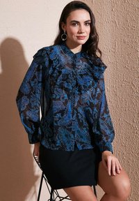 Blue and black patterned blouse with ruffled collar and sleeves, paired with a black skirt. Sheer material and elegant paisley design.