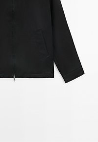Black zip-up jacket with a side pocket and long sleeves, shown against a white background.