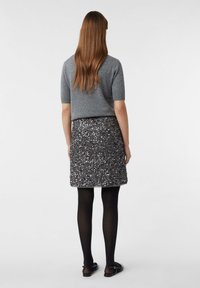 Szary sweter z krótkim rękawem w połączeniu z czarną spódnicą z cekinami, czarnymi rajstopami i czarnymi sandałami, widoczny od tyłu.