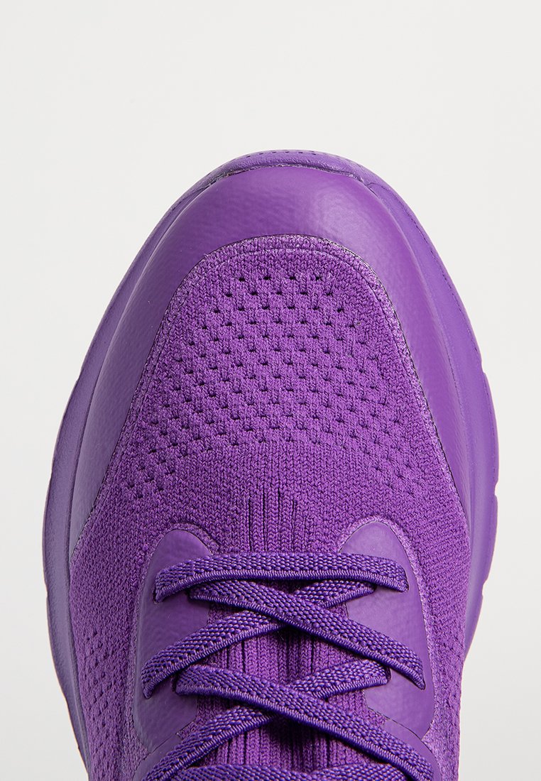 Scarpa da ginnastica viola con tomaia in tessuto a maglia, lacci abbinati e punta arrotondata liscia su uno sfondo chiaro e semplice.