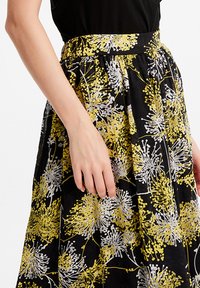 Jupe à motif floral avec de grands designs jaunes et blancs sur fond noir. Fabriquée en tissu léger avec une taille froncée.