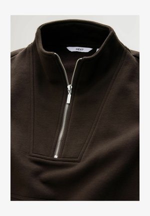 Brown pullover with a high collar, featuring a silver zipper and flatlock seams. Made of soft material, it has a structured, clean design.