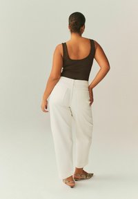 Ruskea hihaton paita yhdistettynä korkeavyötäröisiin, valkoisiin leveälahkeisiin housuihin. Tekstuurilliset, kärjestä teräväkärkiset kengät, joissa on käärmekuvio.