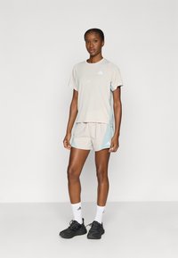 Αθλητική μπλούζα και σορτς σε ανοιχτό μπεζ χρώμα με ανοιχτές γαλάζιες πινελιές. Περιλαμβάνει λεπτομέρειες με λογότυπο και χαλαρή εφαρμογή. Συνδυάζεται με μαύρα αθλητικά παπούτσια.