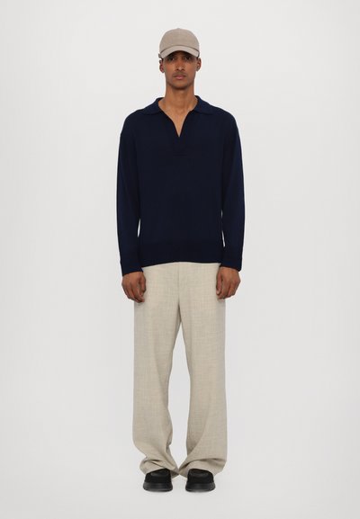 Maglione a maniche lunghe blu navy con colletto, pantaloni a gamba larga color beige chiaro e scarpe nere; persona che indossa un cappello beige. Design semplice e pulito.