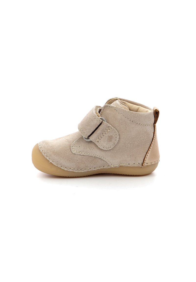 Botín de ante beige con una correa de velcro, puntera redondeada y suela de goma clara. Presenta costuras sin costura y un pequeño tirador en la parte trasera.