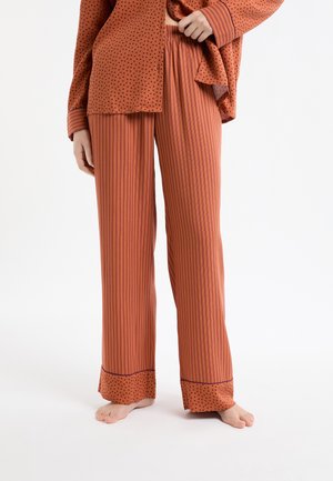 Piżama w kolorze rdzy, składająca się z koszuli w kropki oraz spodni w paski z wzorzystym mankietem. Materiał jest lekki, o luźnym kroju.