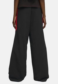 Pantalons larges noirs en tissu doux, dotés d'une bande latérale rouge contrastante et d'une taille élastiquée. Design simple avec des lignes épurées.