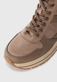 Rudi suede sportiniai bateliai, turintys apvalų pirštą, tekstūruotą paviršių, sustiprintą siuvimą ir guminį padu su šviesiomis juostelėmis. Raišteliai rudi.